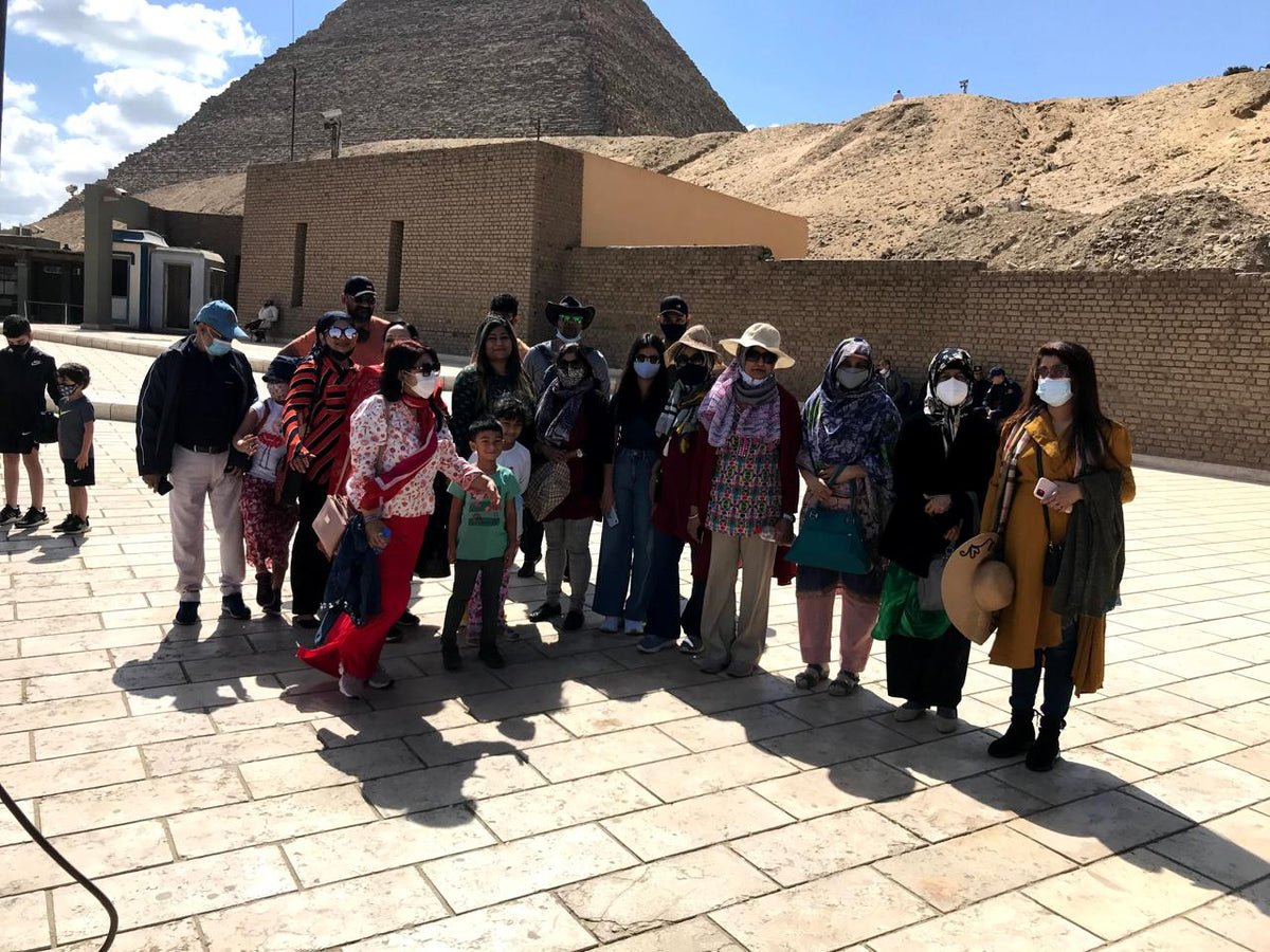 Khonsutours Gästegruppe sitzt entspannt vor den Pyramiden von Gizeh mit Kairo im Hintergrund